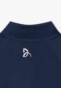 Primo piano di un collo alto blu navy con logo stilizzato bianco centrato sotto la linea del collo su una superficie di tessuto liscia.