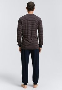 Langsleeve gestreept top in donkere tinten met marineblauwe pyjamabroek. Zachte stof, relaxte pasvorm, geribbelde manchetten en tapered broekspijpen.