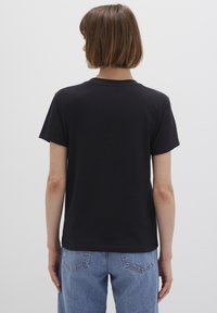 Black cotton t-shirt with a round neckline and short sleeves, featuring a slightly loose fit. Displayed from the back, paired with light blue jeans.
