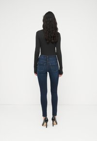 Σκούρο τζιν skinny με ψηλή μέση, διαθέτει δύο πίσω τσέπες και μεσαίο ξέβγαλμα. Συνδυασμένο με μαύρα παπούτσια με τακούνι.