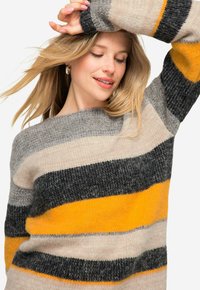 Maglione lavorato a maglia con strisce orizzontali in grigio, giallo senape e beige. La consistenza è morbida e accogliente, con un ampio scollo e maniche larghe.