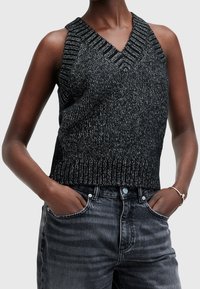 Svart ärmlös stickad topp med V-ringning, ribbad fåll och texturerat mönster, kombinerad med mörkgrå högmidjade jeans.