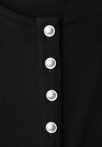 Gros plan sur un tissu noir côtelé avec quatre boutons décoratifs argentés alignés verticalement sur une patte de boutonnage avant.