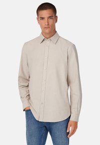 Camisa color beige claro de botones con cuello clásico, mangas largas y una textura suave. Presenta un dobladillo recto y botones en contraste.