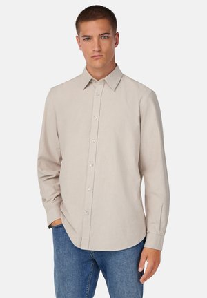 Camisa color beige claro de botones con cuello clásico, mangas largas y una textura suave. Presenta un dobladillo recto y botones en contraste.
