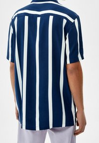 Camicia a maniche corte con strisce verticali blu navy e bianche, orlo dritto e colletto classico, realizzata in tessuto leggero.