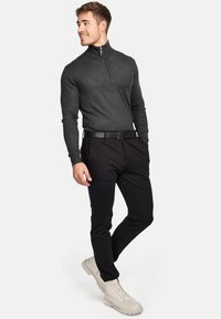 Grå, langærmet, lynlås-top kombineret med sorte, slim-fit bukser. Har et sort bælte og lysfarvede, slidstærke ankelstøvler.