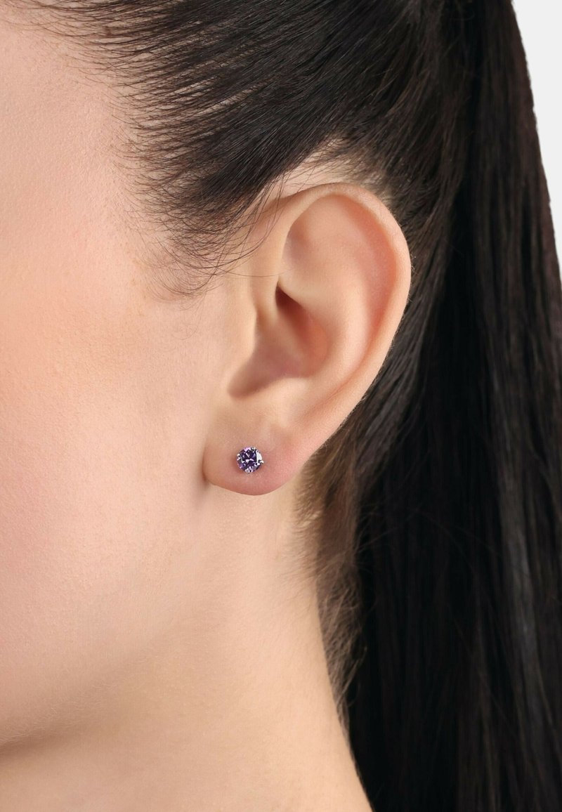 Lila ädelstensstiftörhänge i rund form, med en slät metallinställning. Den blanka ytan kompletterar örats naturliga kontur.