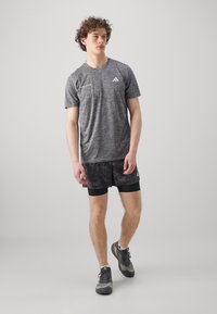 T-shirt de sport gris avec une finition texturée, associé à un short noir à motifs et des chaussures de sport grises. Design décontracté et ajusté.