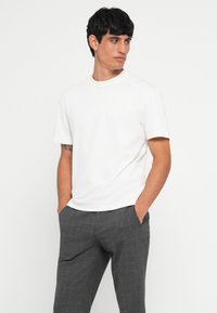 Witte t-shirt met korte mouwen, ronde hals, gecombineerd met grijze geblokte broek. Het t-shirt heeft een gladde textuur; de broek heeft een gestructureerd patroon.