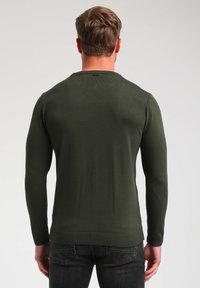 Maglione a maglia verde scuro con maniche lunghe, scollatura tonda e polsini e orlo a costine. Il tessuto appare liscio e ha una forma aderente.