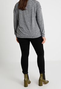 Grijze trui met gespen op de schouders, gecombineerd met zwarte strakke broek en groene enkellaarsjes met hak.