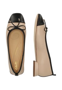 Ballet flats, joissa on beige nahkainen päällinen, musta kärki ja nauha yksityiskohtana. Varustettu pienellä korolla ja kultaisella logolla sisäpohjassa.