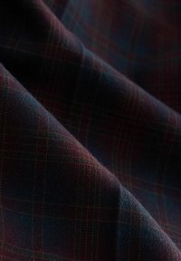Tartan stof in donkerblauw, bordeaux en groen met een geweven ruitpatroon. De textuur lijkt zacht en lichtjes pluizig.