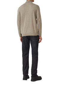 Jasnobeżowy międzydziergany sweter z prążkowanym kołnierzem, długimi rękawami i dopasowanym krojem, zestawiony z czarnymi dżinsami i czarnymi butami.