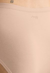 Beige Sloggi undertøj med en glat, elastisk tekstur. Har et lavt liv og flade sømme for komfort. Diskret logo ved linningen.