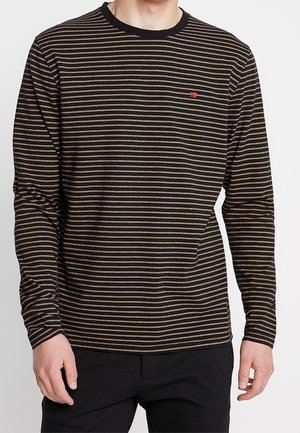 Hombre con una camiseta de manga larga con rayas horizontales negras y marrones y un pequeño logo rojo en el pecho izquierdo.