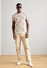 Mønstret T-shirt i flere farver lavet af let stof, parret med beige bomuldsbukser og hvide sneakers. Solbriller fuldender looket.