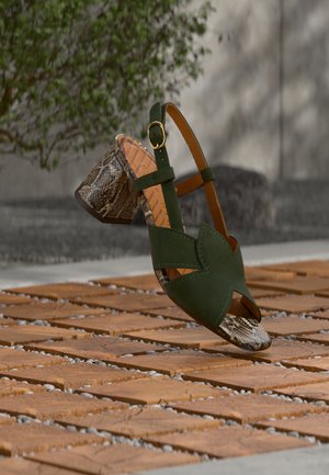 Πράσινο σανδάλι από σουέντ με σχέδιο με κοψίματα, διαθέτει τακούνι με υφή φιδιού και χρυσή αγκράφα σε ρυθμιζόμενο λουράκι αστραγάλου.