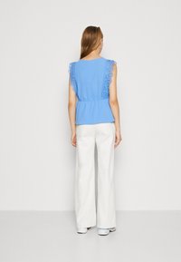 Haut bleu à manches courtes avec accents en dentelle, taille ajustée et coupe décontractée, associé à un pantalon blanc ample et des baskets blanches.