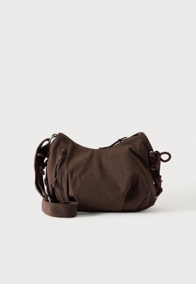 Sac à bandoulière en velours côtelé marron avec sangle réglable, fermeture éclair et détails à cordon latéraux sur fond blanc.