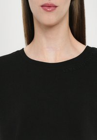 Musta T-paita, joka on valmistettu puuvillasta ja jossa on pyöreä kaula-aukko sekä kohokuvioitu "ARMANI EXCHANGE" -teksti kauluksessa. Sujuva rakenne, rento muotoilu.