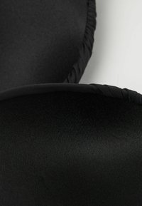 Černá textilní nášivka s hladkým povrchem, zaoblenými okraji a spletaným lemováním, převážně viděná v detailním pohledu.