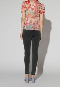 Haut fleuri multicolore avec des manches courtes bouffantes, associé à un jean skinny gris et des sandales à talons carrés bleues. Vue de dos.