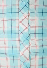 Helle blaue, weiße und rote Karostoff mit passenden hellblauen Druckknöpfen an der vorderen Verschlussleiste des Kleidungsstücks.