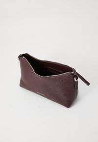 Pochette en cuir bordeaux avec surface texturée, fermeture éclair argentée et branding discret. Présente une ouverture diagonale pour un accès facile.