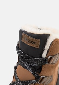Botas de ante marrón y textil negro con un puño de piel sintética, hilos plateados en los cordones y un parche con el logo de Geox en el tobillo.