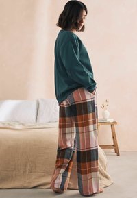 Grøn sweatshirt med løstsiddende pasform, parret med multifarvede ternede bukser i orange, pink og grå. Blødt stof, vidde ben-design.