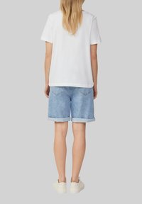 T-shirt en coton blanc, à manches courtes, associé à un short en denim bleu clair, retroussé. Des baskets décontractées complètent la tenue.