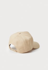 Beige színű pamut sapka ívelt gengével, hat paneles kialakítással, hátul állítható pánttal és párnázott tetejű gomb részletezéssel.