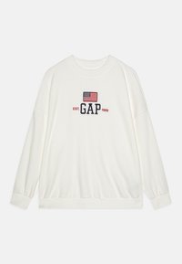 Sudadera blanca de manga larga con un logo "GAP" en navy y una bandera americana bordada encima, cuello redondo y puños elásticos.