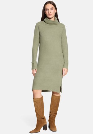 Olivgrünes, langärmeliges Sweatshirtkleid mit Wasserfallausschnitt, gerippten Bündchen und Seitenschlitzen. Kombiniert mit kniehohen Stiefeln aus braunem Wildleder.