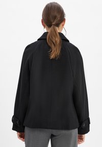 Zwarte wolmix jas met een brede kraag, getailleerde pasvorm en knopenmanchetten. Soepele textuur en een schone, minimalistische uitstraling.