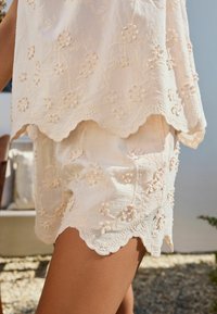 Vit broderad topp med scallopkant och blommönster, tillsammans med matchande shorts med liknande broderi och scallopkanter.