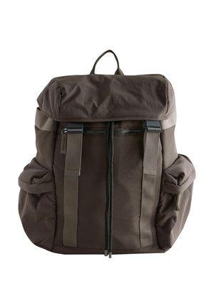 Tumepruun riidest seljakott kaanelehiga, esiküljel luku tasku, kaks küljetaskut, reguleeritavad rihmad ja ülemine käepide.