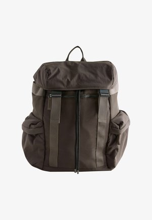 Tumepruun riidest seljakott kaanelehiga, esiküljel luku tasku, kaks küljetaskut, reguleeritavad rihmad ja ülemine käepide.