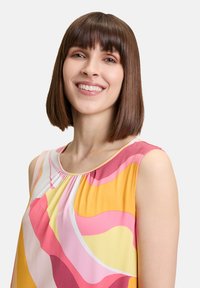 Bezrękawnik z okrągłym dekoltem, charakteryzujący się odważnym, wielokolorowym wzorem fal w odcieniach różu, żółci i pomarańczu na jasnym tle.