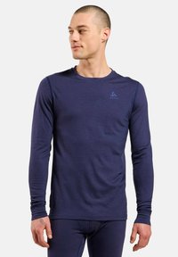 T-shirt de performance à manches longues navy, en tissu léger, col rond, design ajusté, avec un logo discret sur le haut de la poitrine.