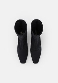 Botines negros hasta el tobillo con un diseño ajustado y elegante. Fabricados en un material elástico, presentan una puntera cuadrada y una textura suave, sin herrajes visibles.