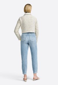 Lettere tekstureret cropped jakke i multifarvet stof; parret med lyseblå jeans og beige sandaler med lav hæl.