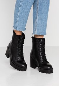 Zwarte leren enkellaarsjes met een bontkraag, veter sluiting, chunky hak en een textured rubberen zool, gecombineerd met lichtblauwe cropped jeans.