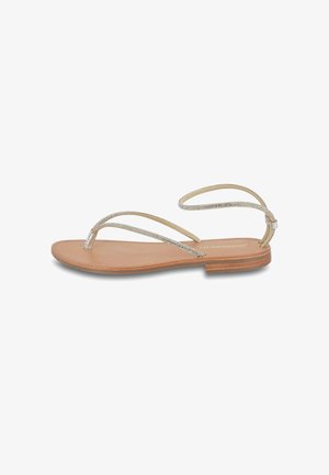 Flat sandal with a tanned leather sole, metallic silver straps, and ankle loop. Minimalist design with a smooth texture.