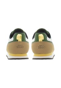 Tenisky mají bílou svrškovou část, zelené akcenty a hnědý semišový podpatek. Žlutá poutka na zadní straně a polstrovaná podrážka. Text říká "OD ROKU 1890."