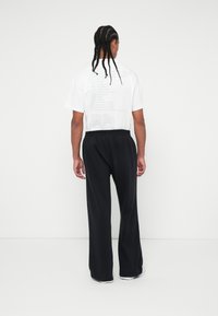 Λευκό T-shirt με κείμενο στο πίσω μέρος, συνδυασμένο με μαύρο, φαρδύ παντελόνι φόρμας. Το ύφασμα φαίνεται μαλακό; το παντελόνι έχει ελαστική μέση και λωρίδες στο πλάι.