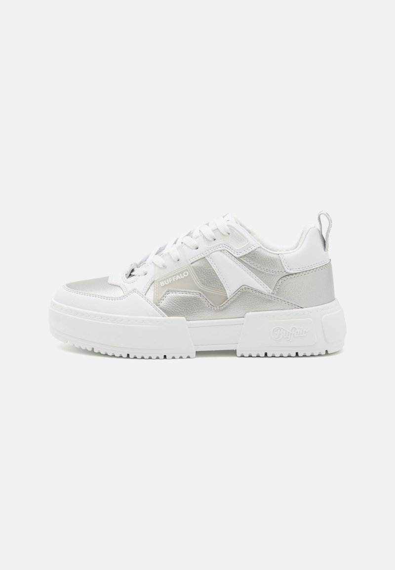 Zapatillas blancas con acentos plateados, que presentan una parte superior texturizada, suela gruesa y un logotipo prominente. Diseño de cordones con un lazo en el talón.