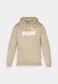Beige Kapuzenpullover mit Kängurutasche, gerippten Bündchen und einem großen weißen "PUMA"-Logo mit einer Puma-Silhouette darüber.